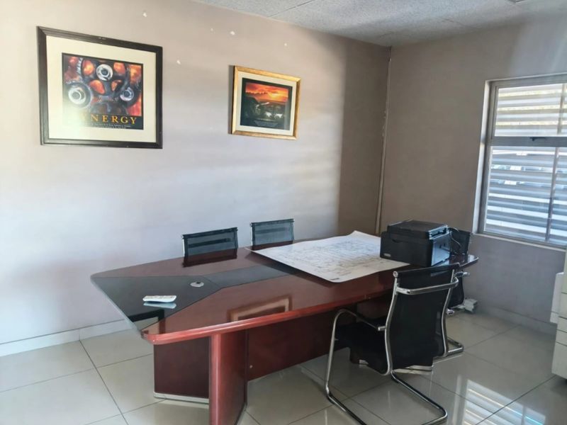 A functional office space featuring tiled flooring, a suspended ceiling, and natural light provided by a window with venetian blinds.