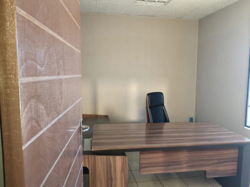 A functional office space featuring tiled flooring and a suspended ceiling, viewed through a solid core door.
