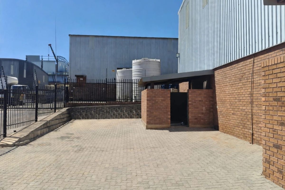 Rear exterior area of the office property featuring brick paving, metal cladding, security fencing, and industrial water storage tanks.