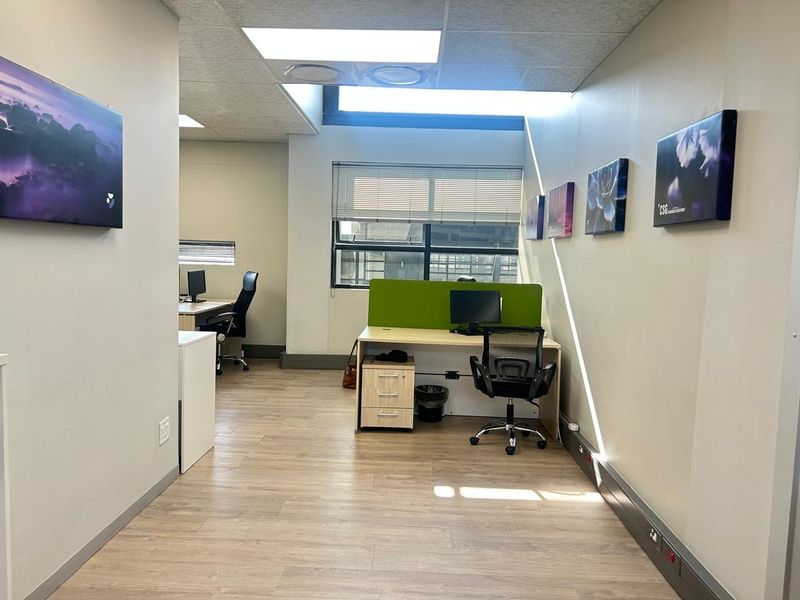 A functional office space featuring laminate flooring, suspended ceilings with recessed lighting, and large windows with blinds providing natural light.