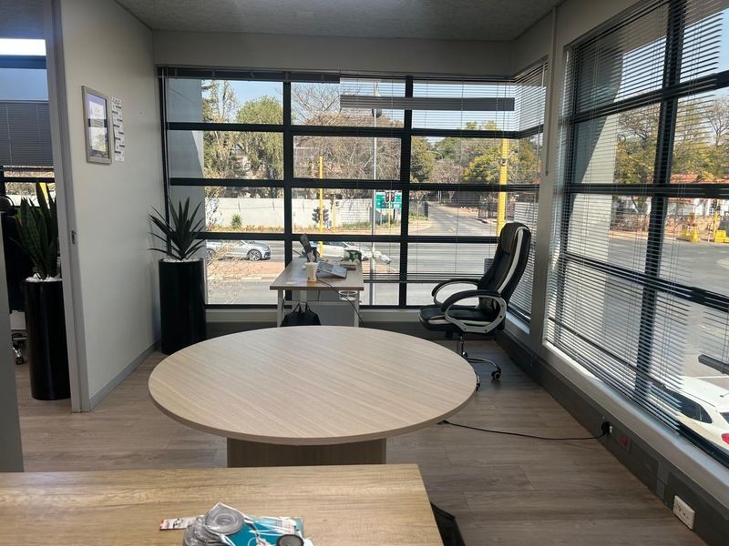 A bright, modern office space featuring large windows with venetian blinds, laminate flooring, and ample natural light.