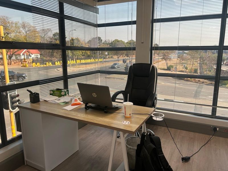 A bright office space featuring large floor-to-ceiling windows with venetian blinds, offering ample natural light and views of the surrounding area.