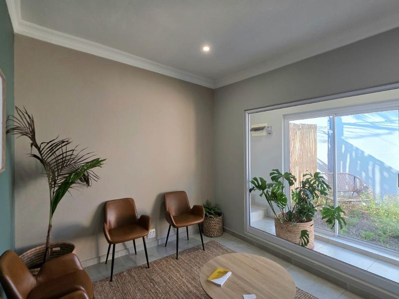 A bright office space featuring tiled flooring, coving, and a large sliding glass door providing natural light and access to an outdoor area.