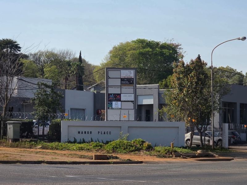 Street view of Manor Place office complex featuring a prominent signage pylon, secure perimeter wall, and gated access.