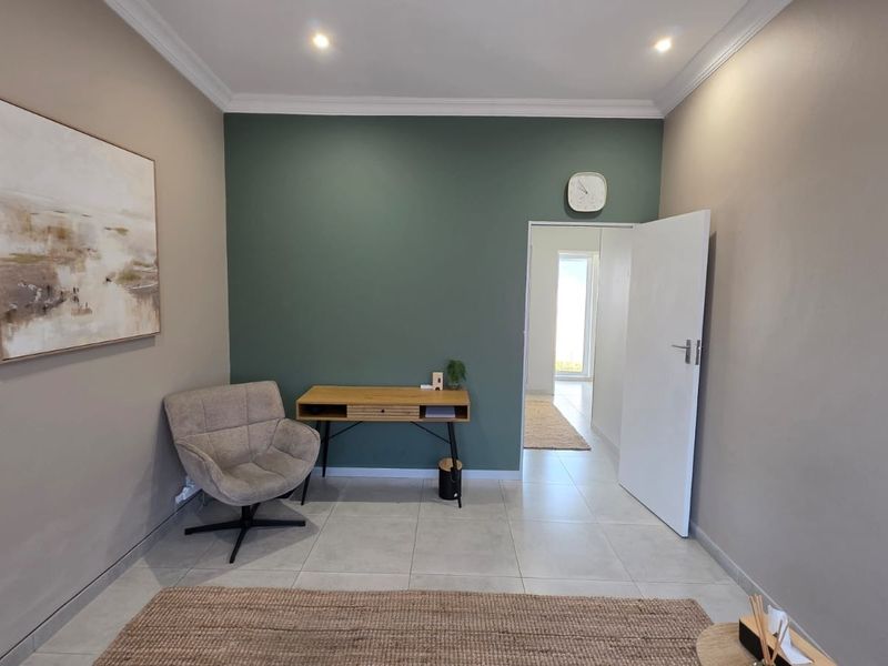 A well-maintained office space featuring neutral walls, a green accent wall, tiled flooring, and recessed downlighting.
