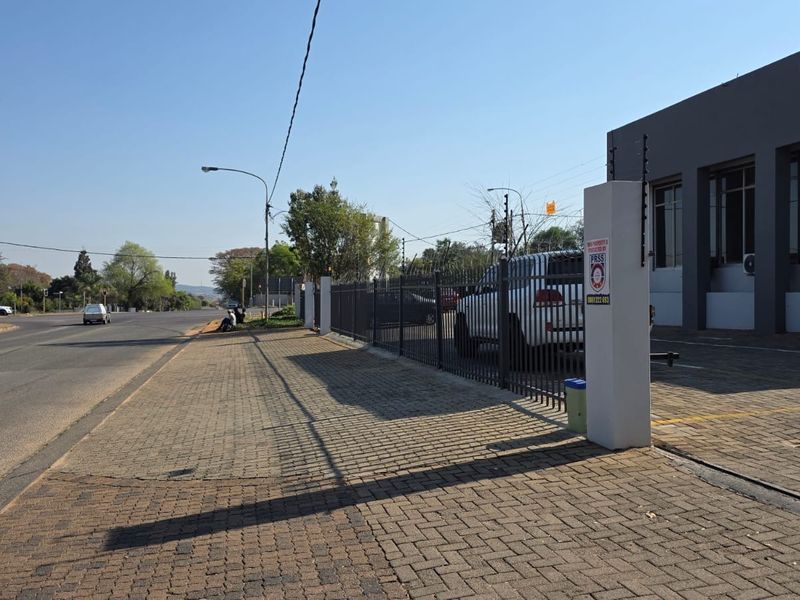 Street-level view of the office property featuring paved driveway access, secure metal perimeter fencing with electric security wires, and concrete boundary pillars.
