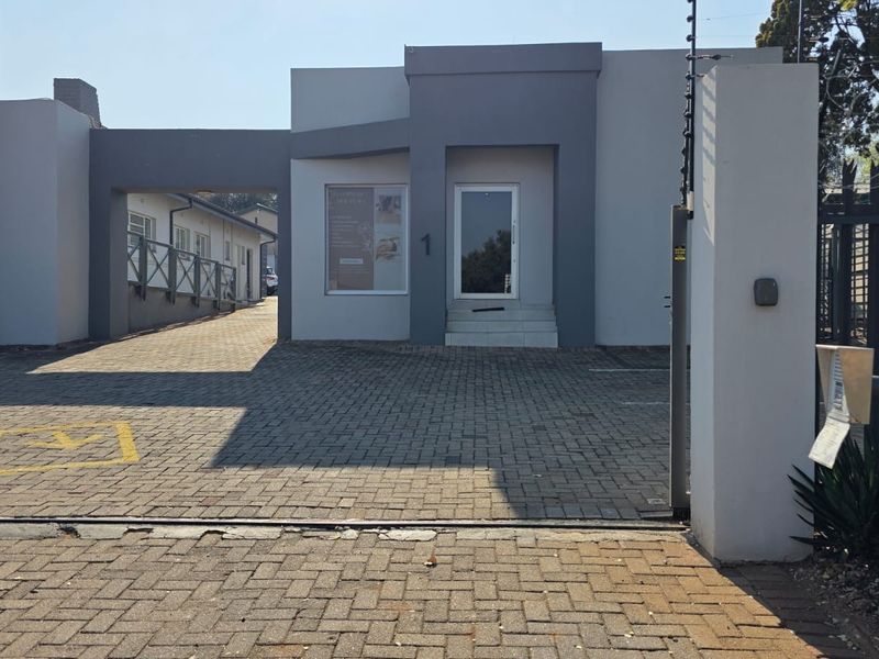 Front exterior view of the office building featuring a paved driveway, secure gated entrance with electric fencing, and a covered walkway.