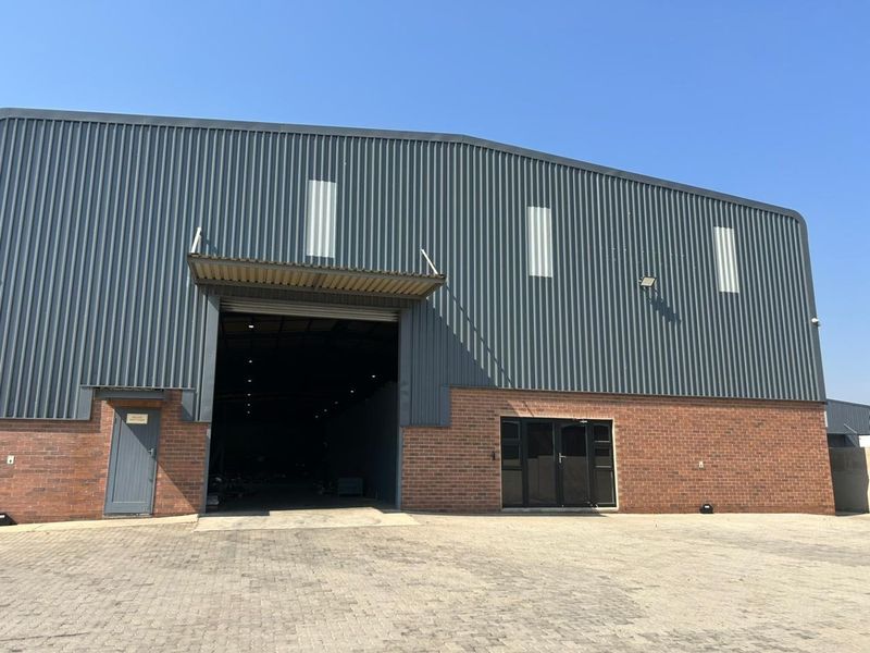 Industrial warehouse exterior featuring a combination of corrugated metal cladding and brickwork, with a large roller shutter door and paved driveway access.
