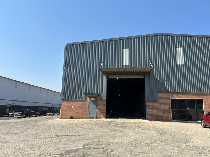 Industrial warehouse exterior featuring corrugated metal cladding, brick base, large roller shutter access, and paved driveway area.