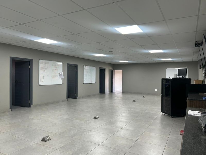 Spacious open-plan office area featuring modern tiled flooring, suspended ceiling with recessed LED lighting, and multiple access points.