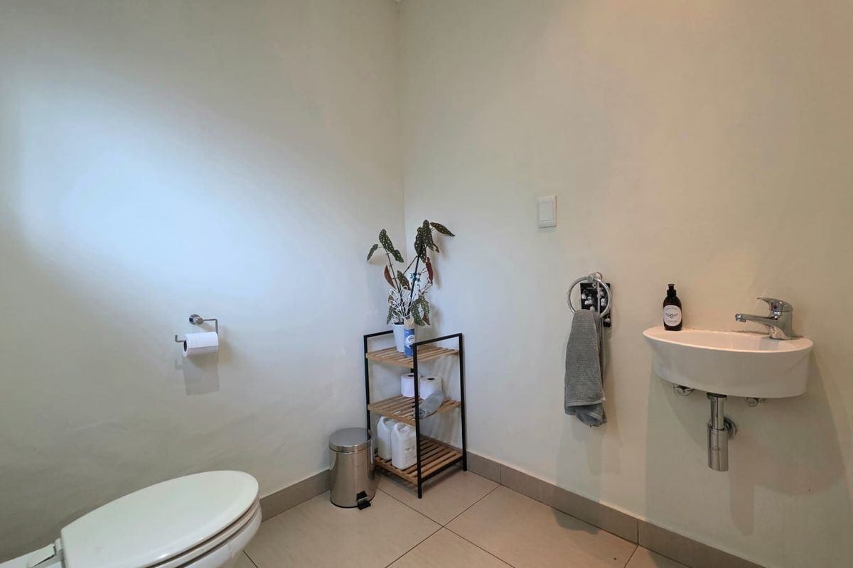 A compact guest bathroom featuring a wall-mounted basin, toilet, and neutral tiled flooring.