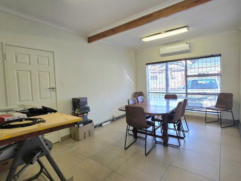 A functional office space featuring tiled flooring, an air conditioning unit, and large windows with security bars, providing a practical work environment.
