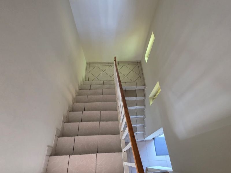 A functional tiled staircase featuring a wooden handrail and vertical balustrade, illuminated by recessed wall windows.