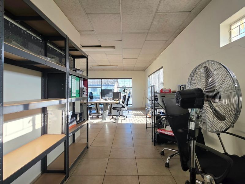 A functional office space featuring tiled flooring, a suspended ceiling, and large windows providing natural light.