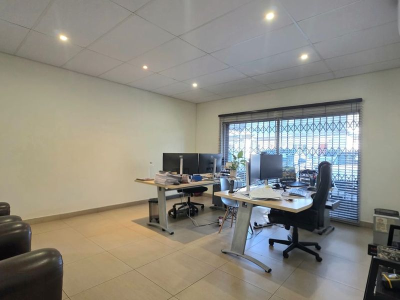 A functional office space featuring tiled flooring, a suspended ceiling with recessed lighting, and an air conditioning unit, providing a professional work environment.