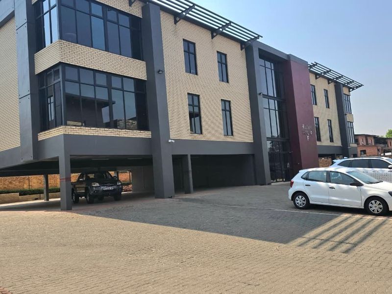Modern multi-story office building featuring a brick and glass facade with a convenient ground-level covered parking area and paved driveway.
