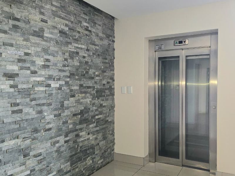 Modern office building lobby entrance featuring a stainless steel elevator and a decorative stacked stone feature wall.