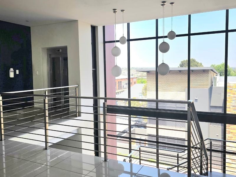 Modern office building hallway featuring a stainless steel balustrade, floor-to-ceiling windows with natural light, and access to a passenger elevator.