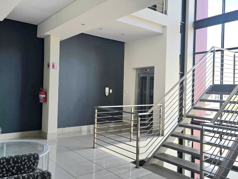 Modern office building entrance featuring a sleek stainless steel staircase, elevator access, and large windows providing ample natural light.