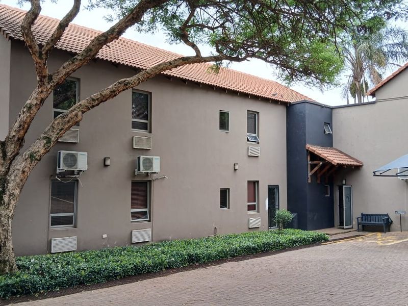 Exterior view of a multi-story office building featuring a paved driveway, shade sail parking, and established landscaping.
