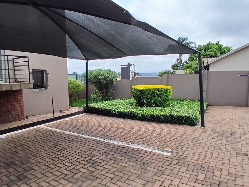 Paved parking area featuring a shade cloth carport structure, landscaped garden bed, and secure boundary walling.