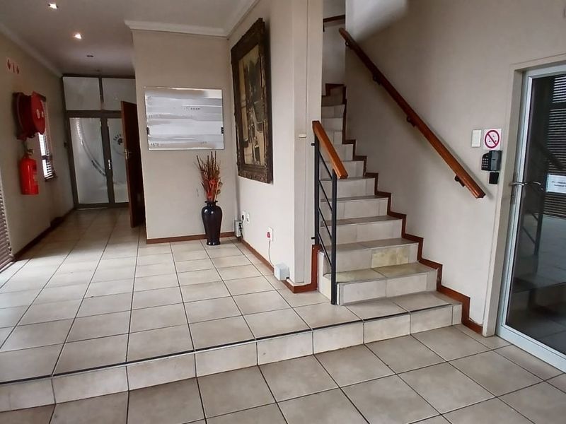 A spacious office building entrance featuring tiled flooring, a central staircase with a wooden handrail, and glass-paneled access doors.