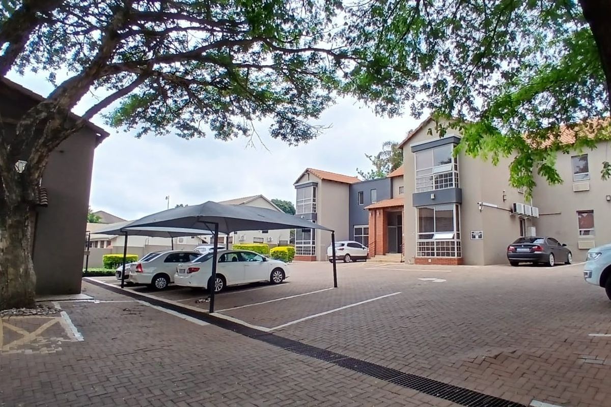 Exterior view of an office complex featuring a paved parking area, covered carports, and multi-story building facades with integrated air conditioning units.