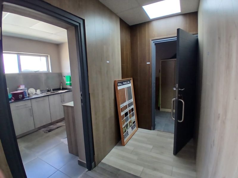 A modern office hallway featuring wood-look wall paneling, tiled flooring, and recessed ceiling lighting, providing access to adjacent office or utility rooms.