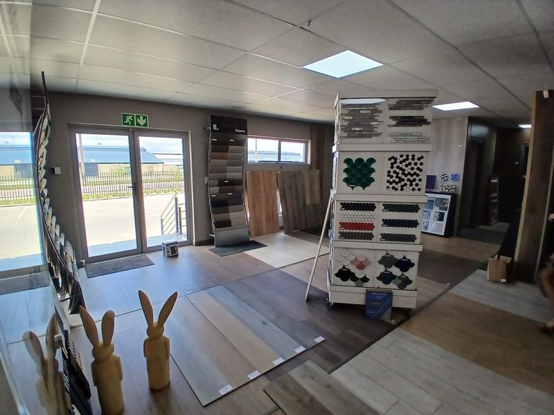 A commercial office showroom space featuring suspended ceilings, recessed lighting, and durable laminate flooring with a glass entrance door.