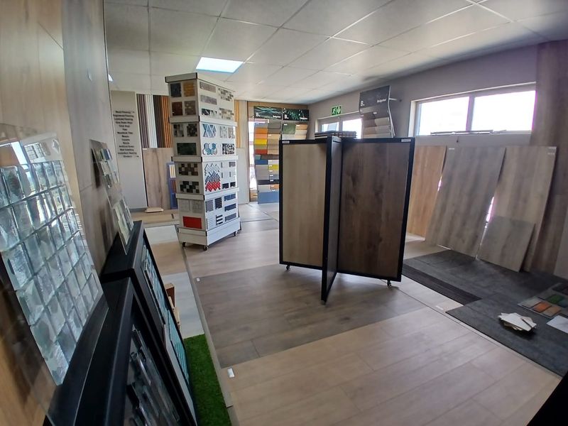 A commercial office space currently utilized as a showroom for flooring and tile samples, featuring a suspended ceiling and ample natural light.