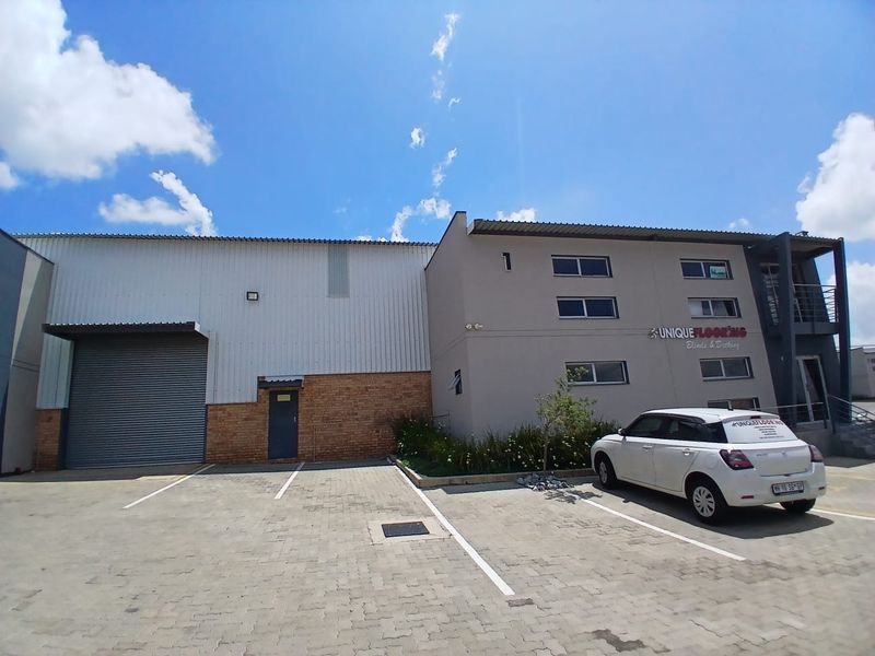 Front exterior view of a commercial office and warehouse facility featuring a roller shutter door, paved parking, and multi-level office space.