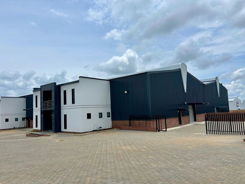 Modern industrial facility featuring a combination of corrugated metal cladding, brickwork, and a spacious paved driveway with secure perimeter fencing.