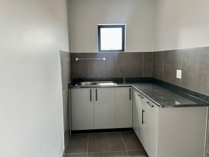 A clean, modern scullery featuring built-in cabinetry, granite countertops, a stainless steel sink, and neutral tiled finishes.