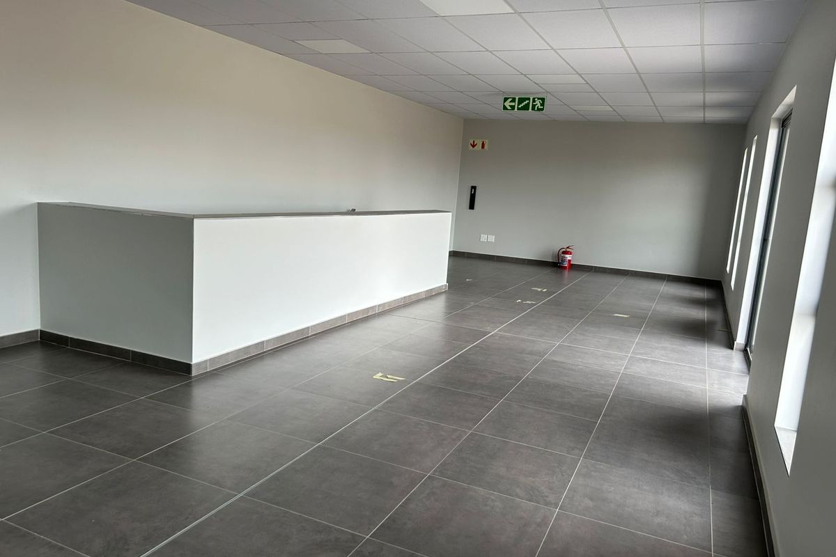 A clean, open-plan industrial office space featuring modern grey floor tiles, a suspended ceiling, and a built-in partition wall.