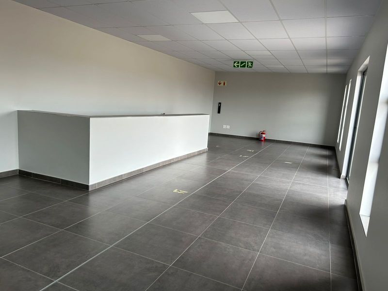 A clean, open-plan industrial office space featuring modern grey floor tiles, a suspended ceiling, and a built-in partition wall.