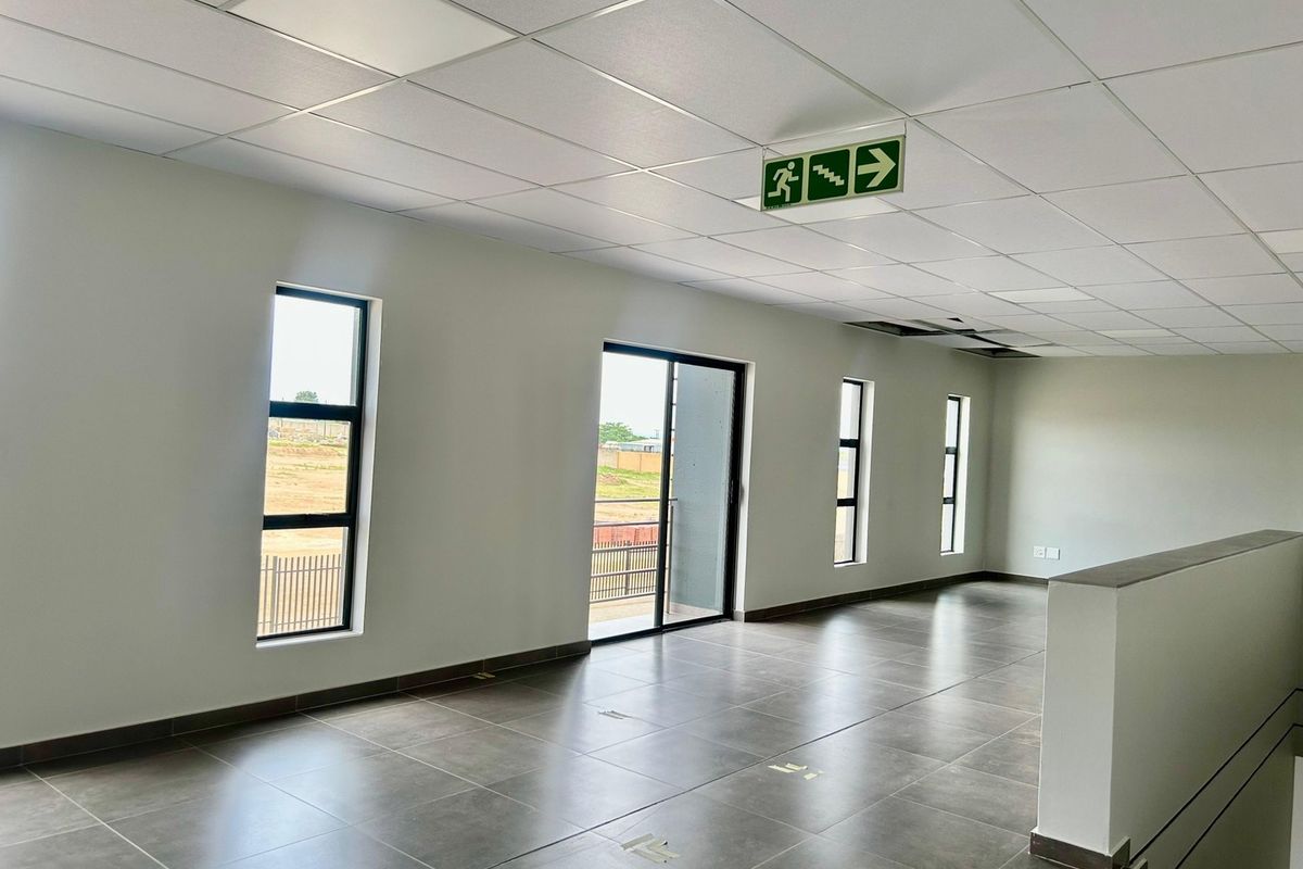 Spacious open-plan office area featuring tiled flooring, suspended ceilings, and large windows providing natural light and access to a balcony.