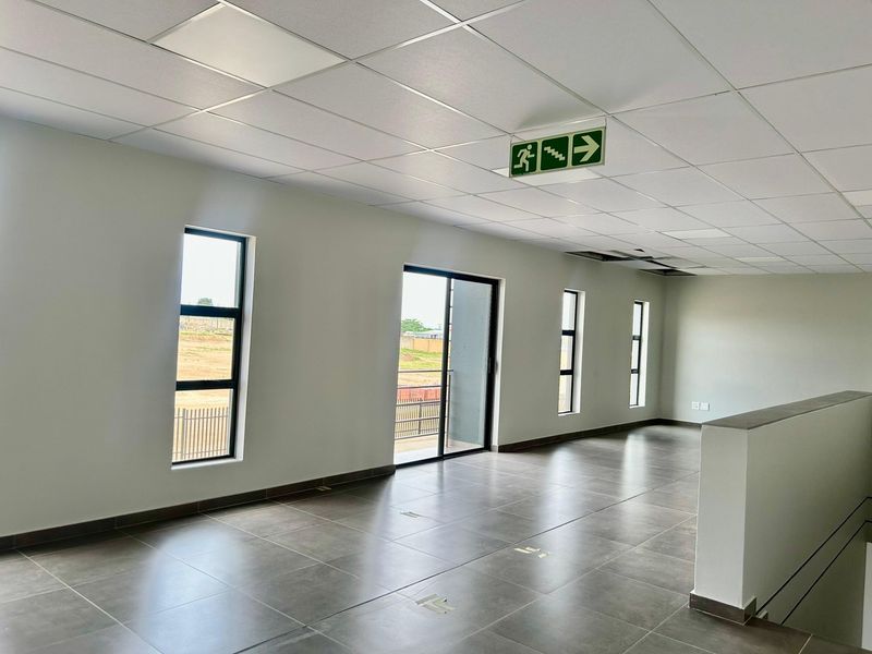 Spacious open-plan office area featuring tiled flooring, suspended ceilings, and large windows providing natural light and access to a balcony.