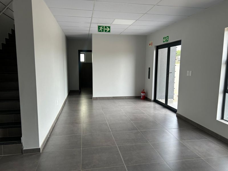 A clean, modern industrial hallway featuring neutral tiled flooring, a suspended ceiling, and direct access to an exterior entrance via glass doors.