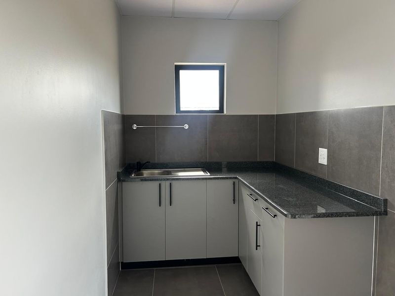 A clean, modern scullery featuring grey built-in cabinetry, granite countertops, a stainless steel sink, and neutral tiled finishes.