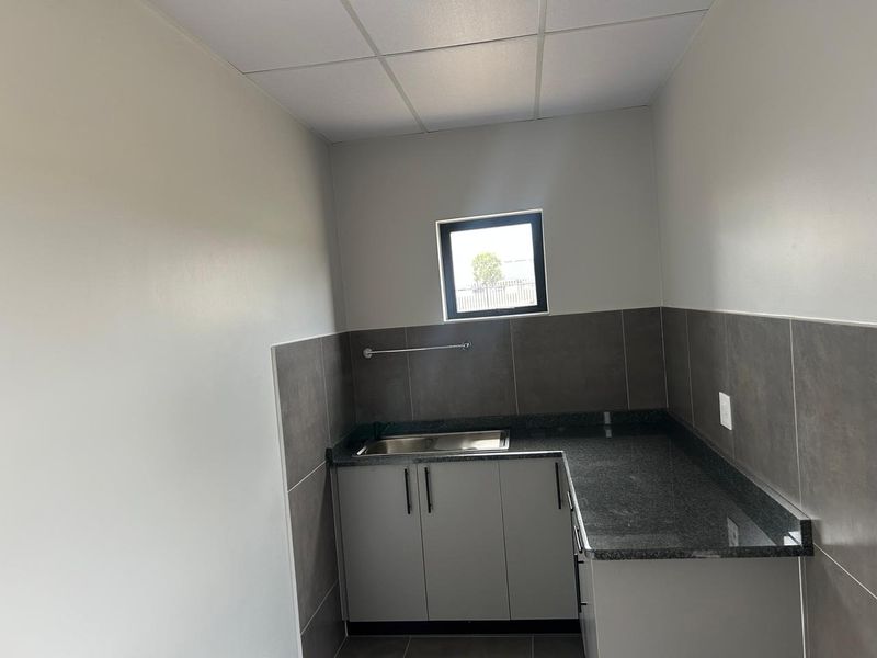 A clean, modern kitchenette featuring granite countertops, built-in cabinetry, a stainless steel sink, and a tiled backsplash in an industrial setting.