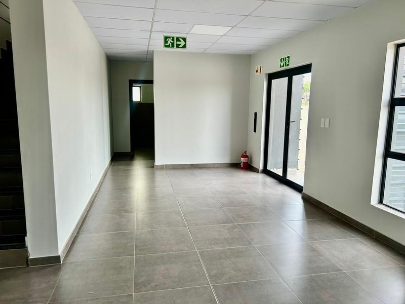 A clean, modern industrial hallway featuring neutral tiled flooring, a suspended ceiling, and direct access to an exterior entrance through glass doors.