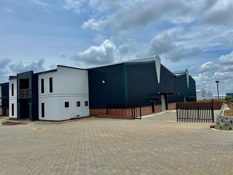 Modern industrial warehouse facility featuring a combination of corrugated metal cladding and brick masonry, with a paved driveway and secure gated entrance.