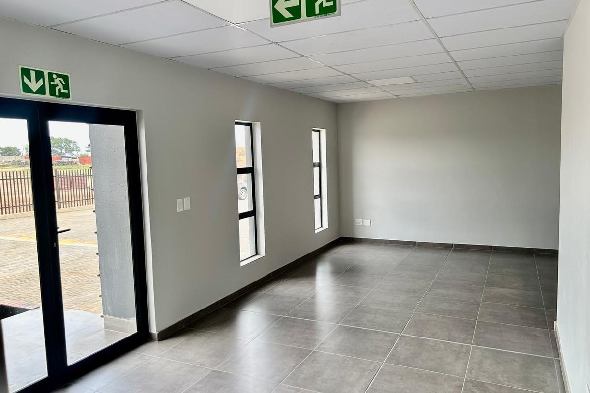 A clean, modern, and empty office space featuring large windows, tiled flooring, and a suspended ceiling with integrated emergency exit signage.