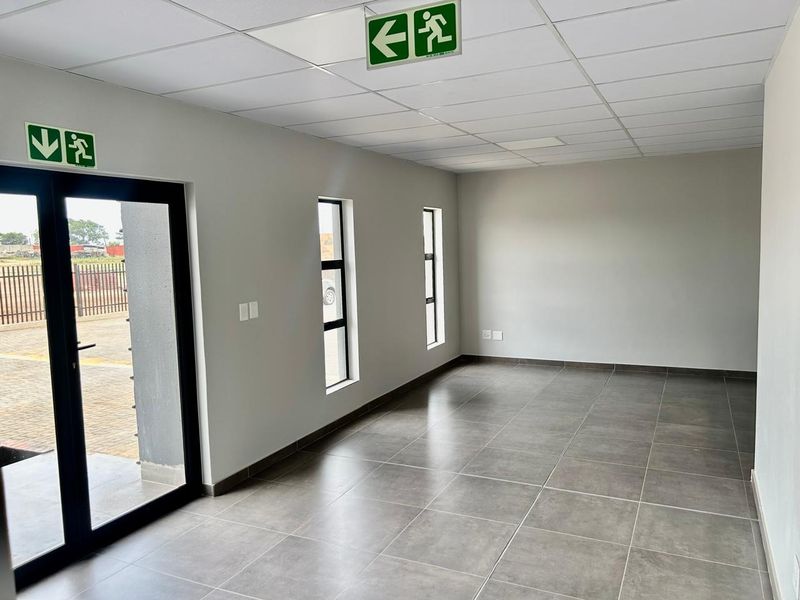 A clean, modern, and empty office space featuring large windows, tiled flooring, and a suspended ceiling with integrated emergency exit signage.