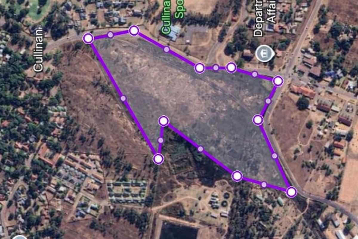 An aerial view of a large, undeveloped commercial vacant land plot with marked boundaries, situated in a developed urban area.