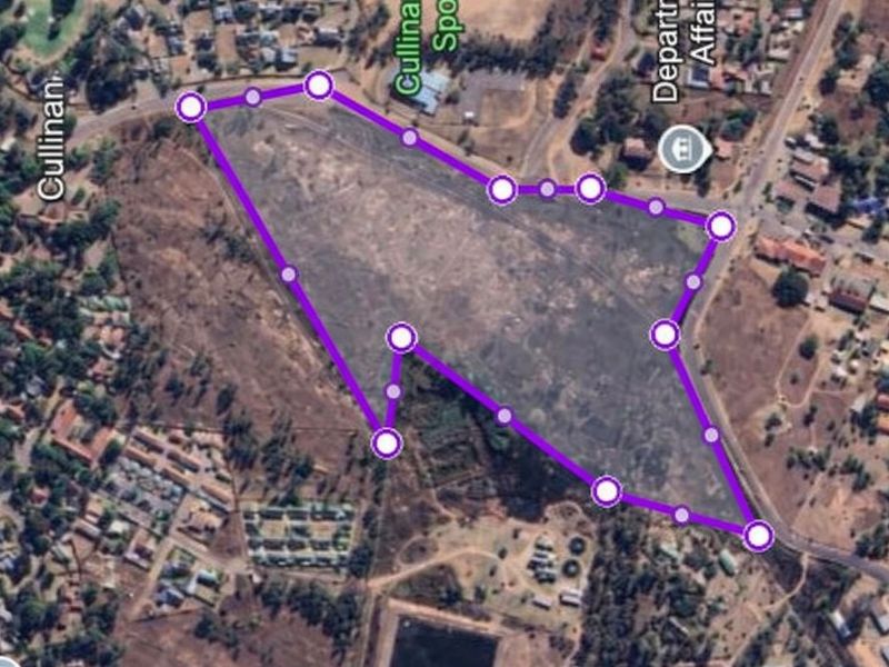 An aerial view of a large, undeveloped commercial vacant land plot with marked boundaries, situated in a developed urban area.