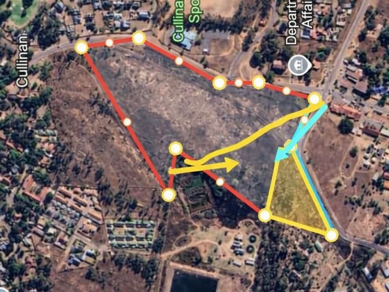 Aerial view of a vacant commercial land plot with superimposed boundary lines and directional markers indicating site layout.