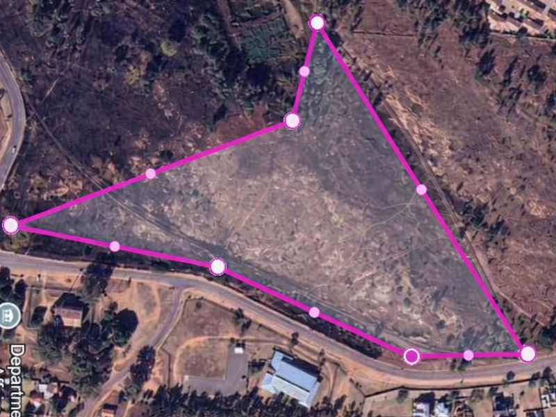 An aerial view of a vacant commercial land plot with marked boundaries, showing surrounding road access and nearby infrastructure.