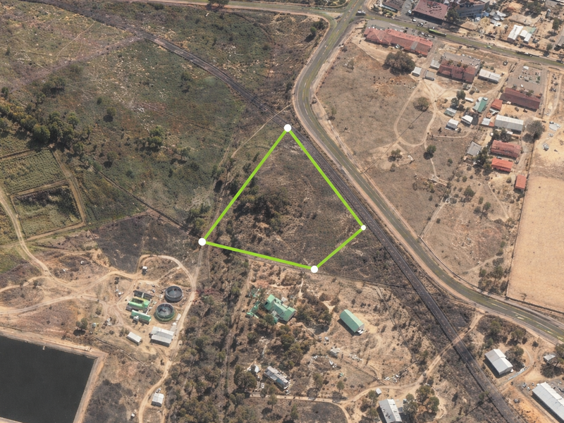 Aerial view of a vacant commercial land parcel with highlighted boundary lines, situated near road infrastructure and surrounding industrial or rural development.