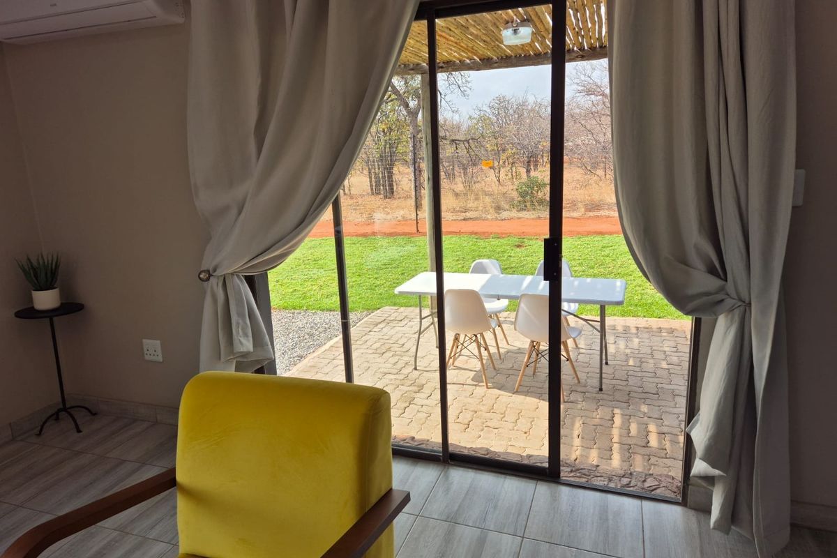 A bright living area featuring tiled floors and a large sliding glass door that opens onto a paved patio with garden views.